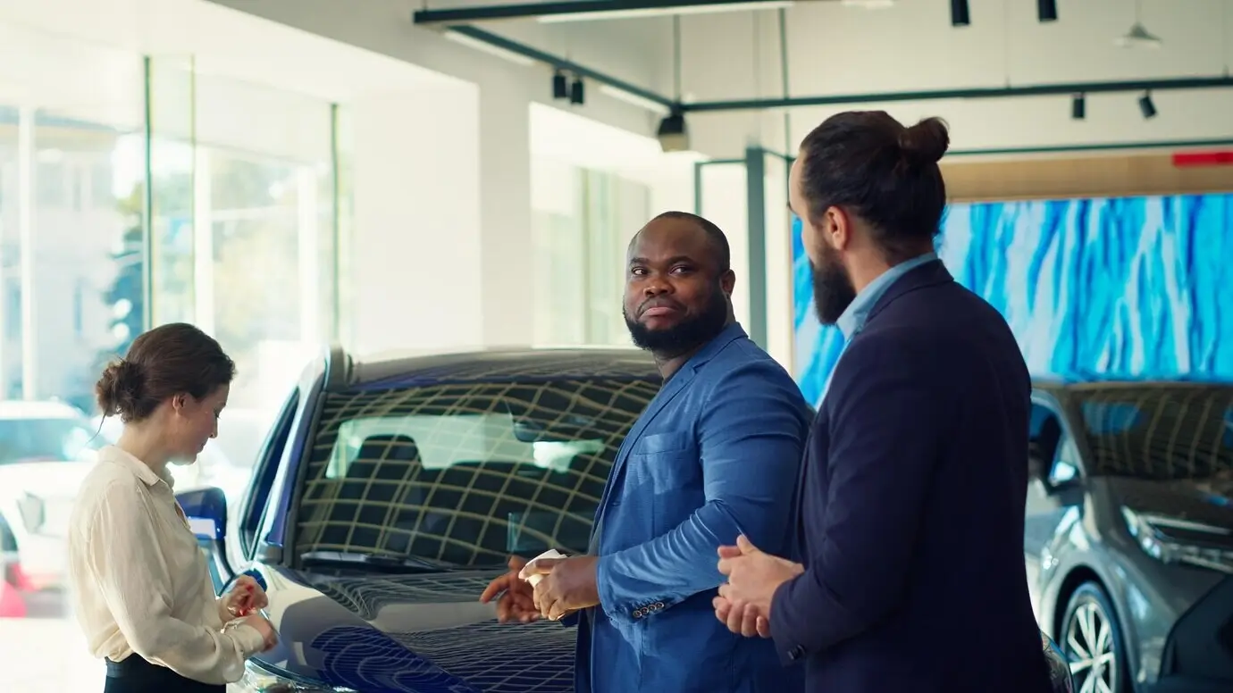 Clients arriving at a car dealership are greeted by a friendly car salesman.