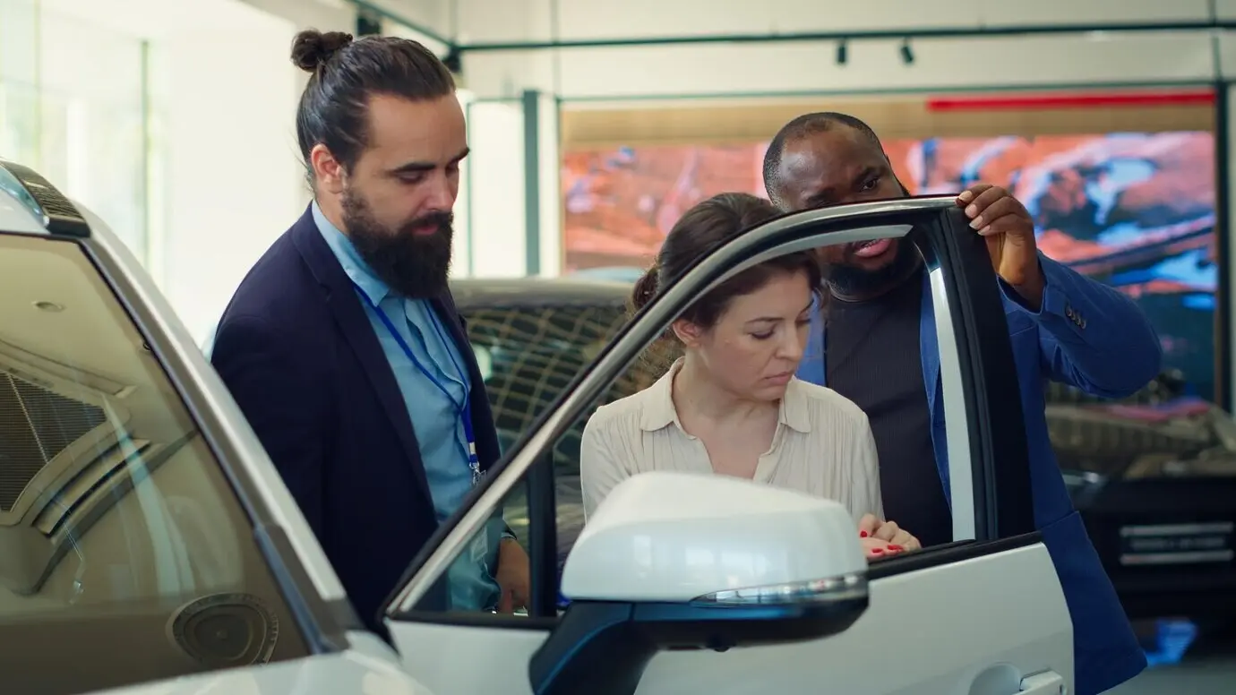 Car dealership representative showing the durability of a vehicle door to clients.